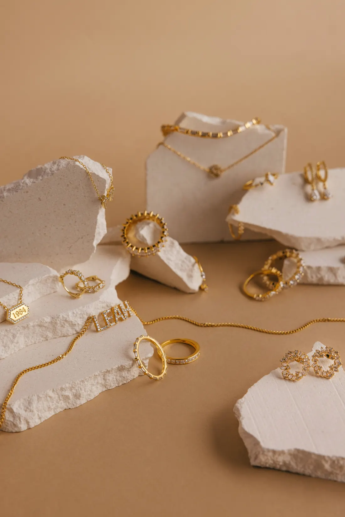 Gold rings, necklaces and earrings styled on cream stone